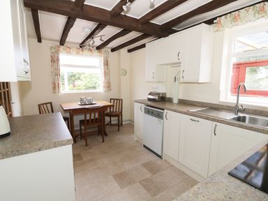 A kitchen with white cabinets a wooden table and chairs under a window at Causeway Cottage in Pencombe