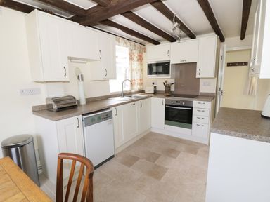 A kitchen with white cabinets a dishwasher oven microwave and a wooden chair at Causeway Cottage in Pencombe