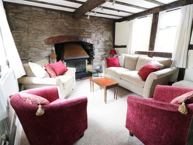 A sitting room with two beige sofas two red armchairs a wooden coffee table and a stone fireplace at Causeway Cottage in Pencombe