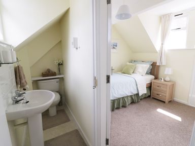 A small bathroom with a toilet and sink next to a bedroom with a single bed and bedside table at Causeway Cottage in Pencombe