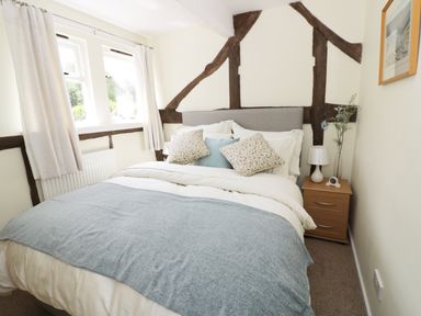 A bedroom with a bed a bedside table a lamp and windows at Causeway Cottage in Pencombe