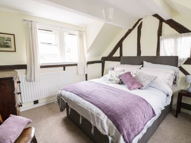 A bedroom with a double bed with purple and floral pillows and a purple throw blanket at Causeway Cottage in Pencombe