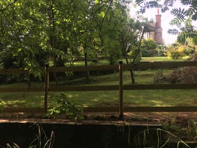A garden with a wooden fence trees and a house in the background at Causeway Cottage Pencombe