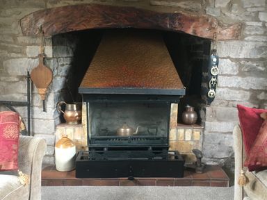 A stone fireplace with a copper hood and various metal pots and a wood bellows at Causeway Cottage in Pencombe