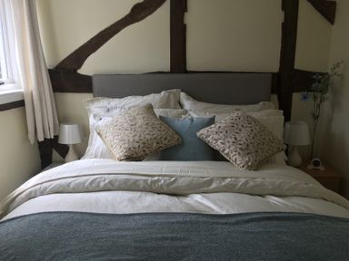 A bed with pillows and blankets between two bedside tables with lamps and a window with curtains at Causeway Cottage in Pencombe