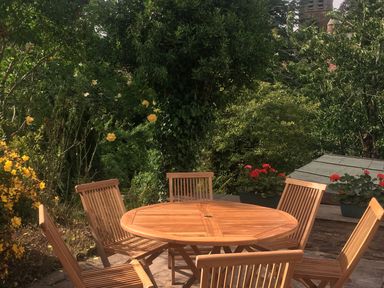A wooden round table with six matching chairs on a patio surrounded by greenery and flowers at Causeway Cottage in Pencombe