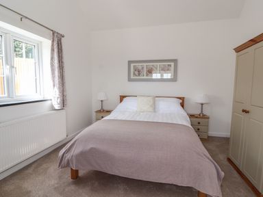 A bedroom with a double bed two bedside tables with lamps a wardrobe and a window at Delfryn in Llannefydd near Denbigh