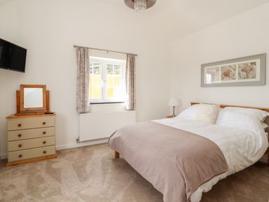 A bedroom with a double bed a dresser with a mirror a wall-mounted television and a window with curtains at Delfryn in Llannefydd near Denbigh