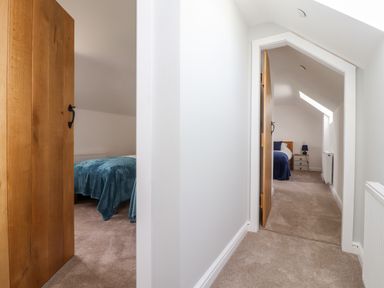 A carpeted hallway with two open wooden doors leading to bedrooms at Delfryn in Llannefydd near Denbigh
