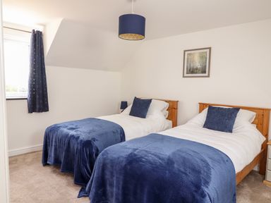 A bedroom with two single beds with blue blankets and pillows a window with blue curtains a lamp hanging from the ceiling and a framed picture on the wall at Delfryn in Llannefydd near Denbigh