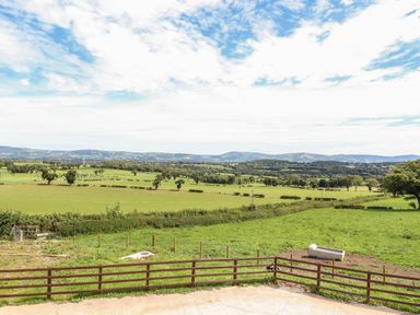 A fenced grassy field with trees and hills in the distance under a partly cloudy sky at Delfryn in Llannefydd near Denbigh