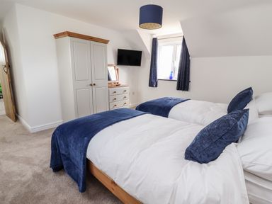 A bedroom with two single beds blue pillows blue throws a wardrobe a chest of drawers and a window with curtains at Delfryn in Llannefydd near Denbigh
