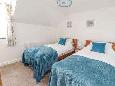 A bedroom with two single beds blue throws and pillows with a nightstand and lamp between the beds at Delfryn in Llannefydd near Denbigh