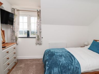 A bedroom with a bed covered in blue blanket beside a window and a dresser with a television at Delfryn Llannefydd near Denbigh