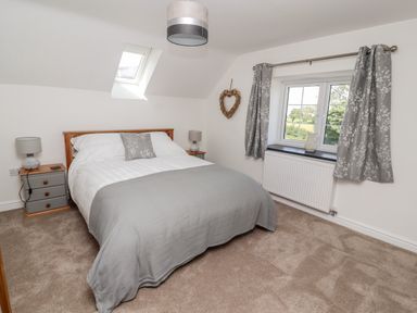 A bedroom with a bed bedside tables lamps window with curtains and a skylight at Delfryn in Llannefydd near Denbigh