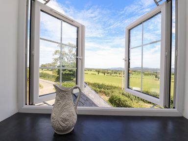 An open window showing fields and trees with a decorative white pitcher on the windowsill at Delfryn in Llannefydd near Denbigh