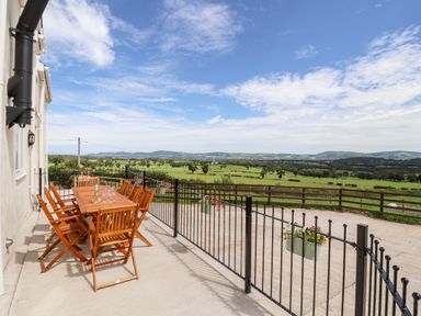 An outdoor patio with a wooden dining table and chairs overlooking a fenced green field at Delfryn in Llannefydd near Denbigh