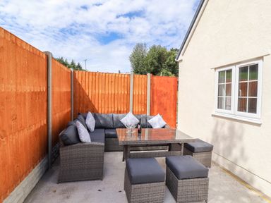 A patio area with a wicker corner sofa with cushions a glass top table and ottoman seats bordered by wooden fences at Delfryn in Llannefydd near Denbigh