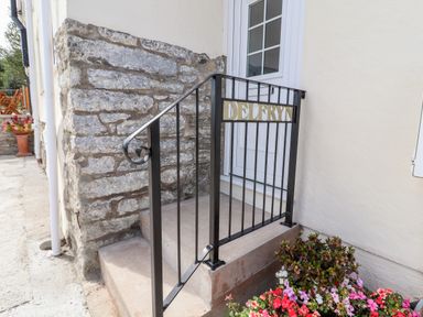 A stone step entrance with a black metal railing featuring the name Delfryn and a flower bed nearby at Delfryn Llannefydd near Denbigh