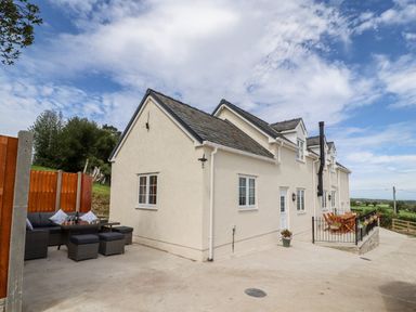 An outdoor seating area with a table and chairs next to a cream building with multiple windows at Delfryn in Llannefydd near Denbigh