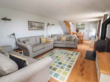 A living room with three sofas and a patterned rug near a dining table and wood stove at Delfryn in Llannefydd near Denbigh