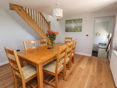 A dining room with a wooden table and six chairs under a staircase at Delfryn in Llannefydd near Denbigh