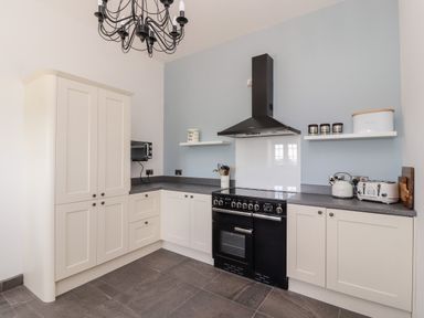A kitchen with white cabinets black stove and hood grey countertops and shelves with containers at Delfryn in Llannefydd near Denbigh