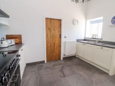 A kitchen with white cabinets, black countertop, a wooden door, and a window above the sink at Delfryn in Llannefydd near Denbigh