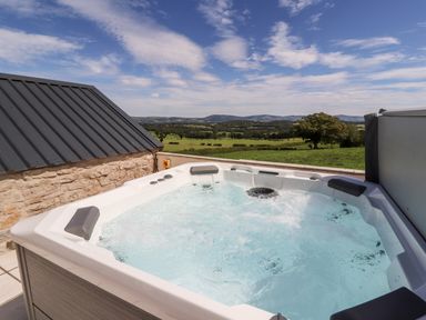 An outdoor hot tub with bubbling water on a patio overlooking green fields and hills at Delfryn Llannefydd near Denbigh