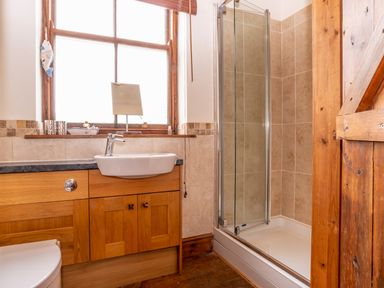 A bathroom with a wooden vanity sink cabinet a glass shower enclosure and a wooden door at The Old School Room in Longhorsley near Morpeth and Alnwick