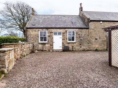 A stone building with a white door and two windows on a gravel driveway at The Old School Room in Longhorsley near Morpeth and Alnwick