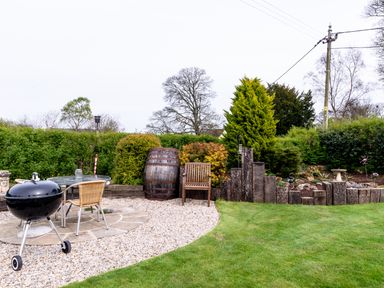 A garden with a barbecue grill table chairs wooden barrel and wooden fence at The Old School Room in Longhorsley near Morpeth and Alnwick