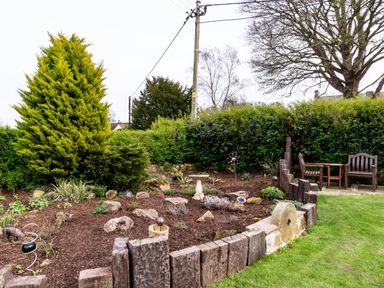 A garden with a flower bed bordered by wooden posts a table and two chairs on grass at The Old School Room in Longhorsley near Morpeth and Alnwick
