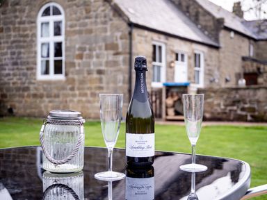 A bottle of sparkling wine and two empty champagne glasses on a table outside a stone building at The Old School Room Longhorsley near Morpeth and Alnwick