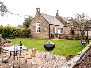 A garden with a stone house lawn table with chairs barbecue and bench at The Old School Room in Longhorsley near Morpeth and Alnwick