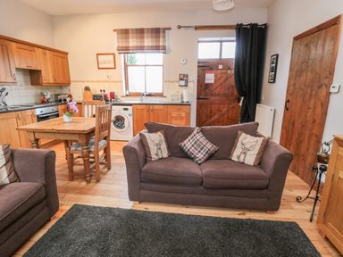 An open-plan kitchen and living area with wooden cabinets a dining table two sofas and a wooden door at The Old School Room in Longhorsley near Morpeth and Alnwick