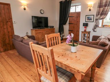 A living room with a wooden dining table and chairs a television on a wooden cabinet and sofas at The Old School Room in Longhorsley near Morpeth and Alnwick