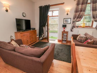 A living room with two brown sofas a wooden TV cabinet with a television a small side table and windows with curtains at The Old School Room in Longhorsley near Morpeth and Alnwick