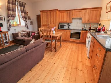 A kitchen with wooden cabinets a dining table with chairs and two sofas at The Old School Room Longhorsley near Morpeth and Alnwick