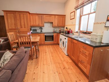 A kitchen with wooden cabinets, a dining table with chairs, a sofa, and appliances with a window at The Old School Room in Longhorsley near Morpeth and Alnwick