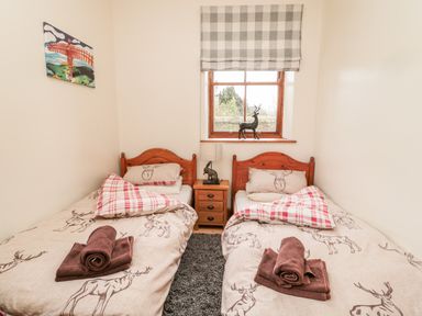 A bedroom with two single beds featuring deer-themed bedding a window with checked blinds and a bedside table with a lamp and a deer figurine at The Old School Room in Longhorsley near Morpeth and Alnwick