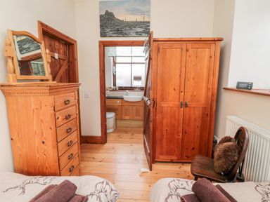 A bedroom with wooden furniture including a wardrobe and chest of drawers and a chair with towels on beds at The Old School Room in Longhorsley near Morpeth and Alnwick