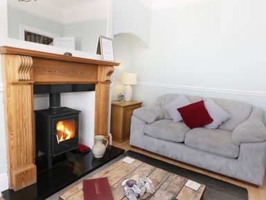 A living room with a wood burning stove fireplace a grey sofa with cushions a wooden coffee table and a side table with a lamp at Number Fifteen in Withernsea