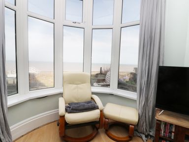 A cream chair with an ottoman in front of bay windows overlooking the sea at Number Fifteen in Withernsea