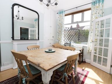 A dining room with a wooden table and chairs a large mirror and a window with patterned curtains at Number Fifteen in Withernsea