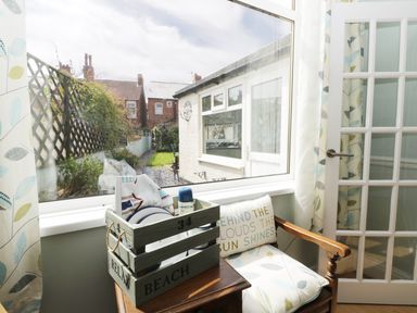 A window view of a garden with a wooden chair and a crate of dishes inside at Number Fifteen in Withernsea