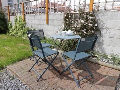 A small outdoor seating area with three blue metal chairs and a round table with a teapot and two cups on a brick patio next to a concrete wall with climbing plants at Number Fifteen in Withernsea
