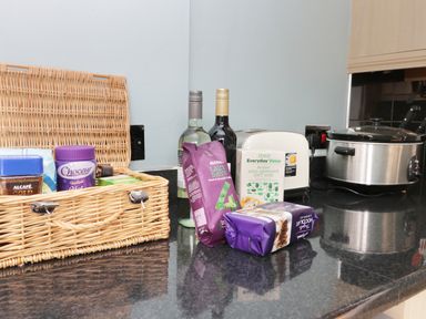 A kitchen countertop with a wicker basket holding coffee jars and other items bottles of wine a carton of milk a toaster a slow cooker and packets of coffee and cookies at Number Fifteen in Withernsea