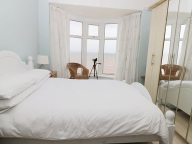 A bedroom with a white bed a wooden chair a telescope by a bay window and a mirrored wardrobe at Number Fifteen in Withernsea