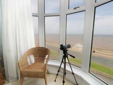A corner with large bay windows overlooking the sea with a wicker chair and a telescope on a tripod at Number Fifteen in Withernsea